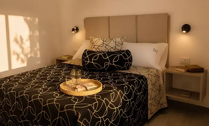 Dormitorio con cama matrimonial, respaldo tapizado, apliques de luz y mesas de luz de madera.